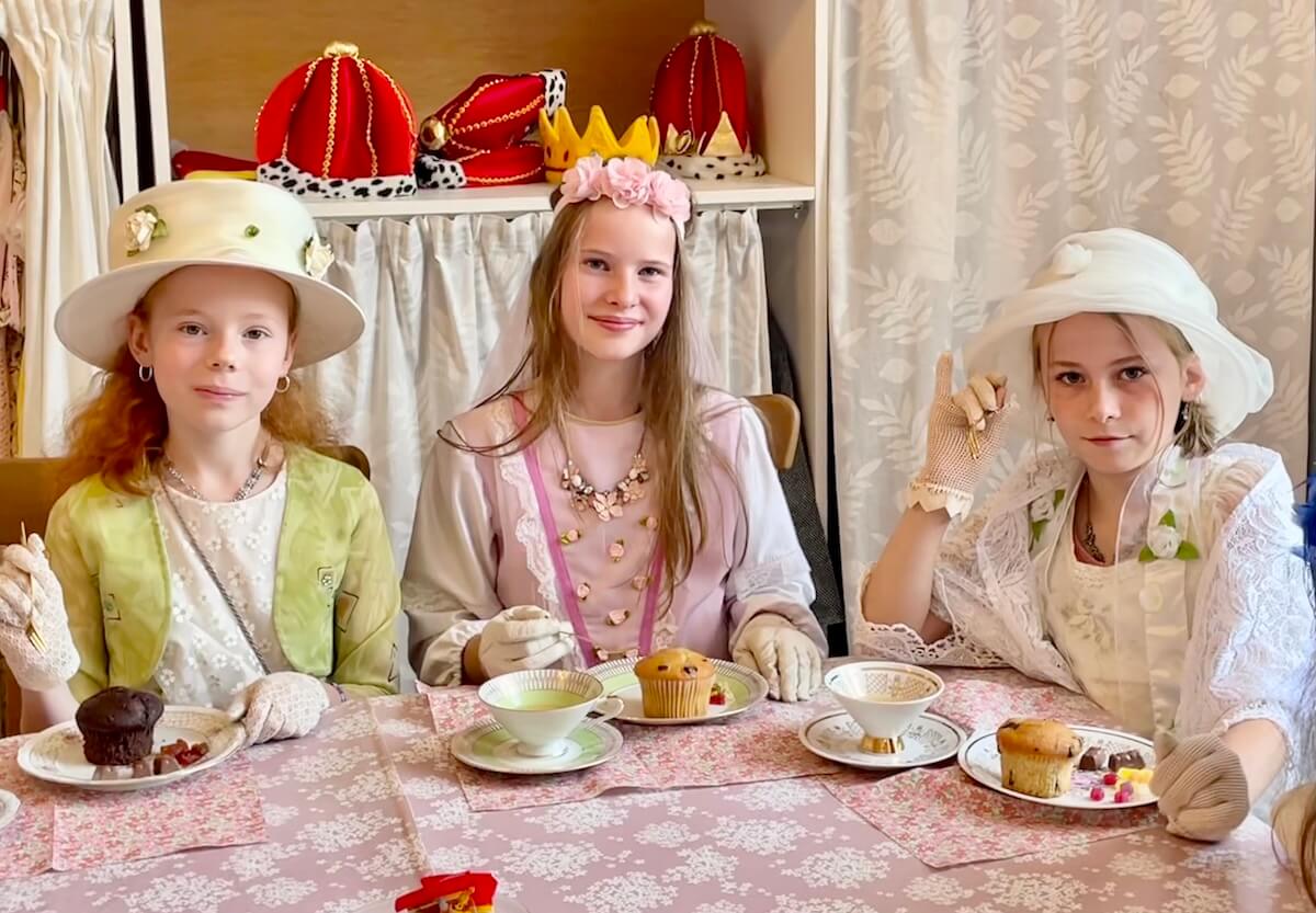 3 Mädchen sitzen festlich gekleidet am Tisch und essen Muffins