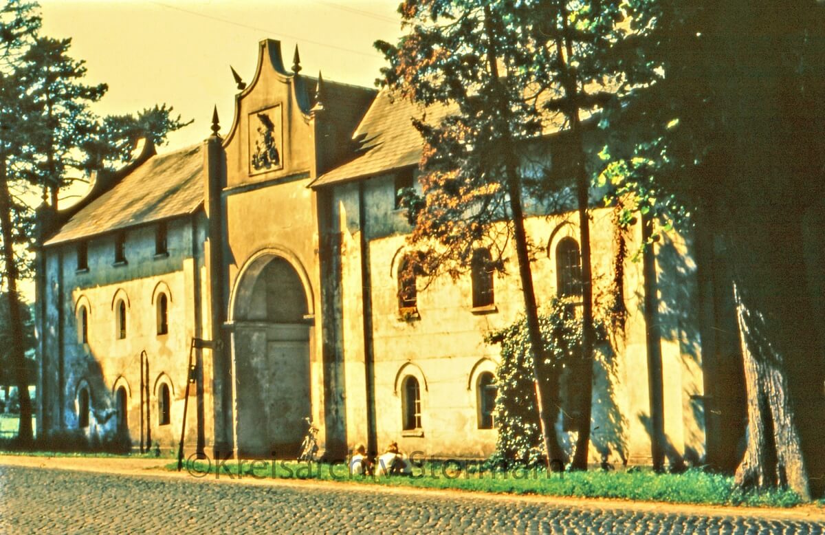 Ein historisches Torhaus an einer Straße, links und rechts Bäume