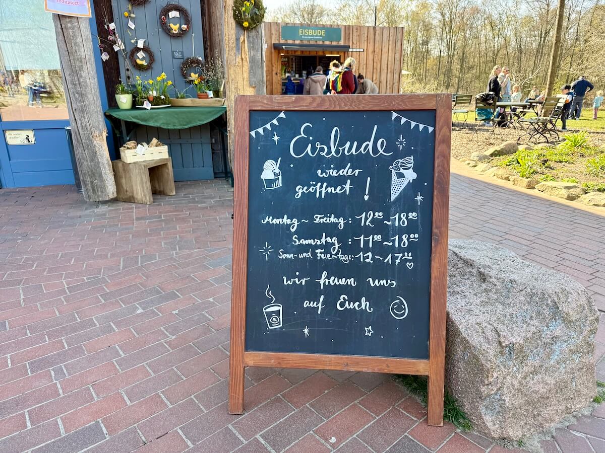 Eine Tafel, auf der die Öffnungszeiten für die Eisbude auf Gut Wulfsdorf stehen, im Hintergrund der Eisverkauf