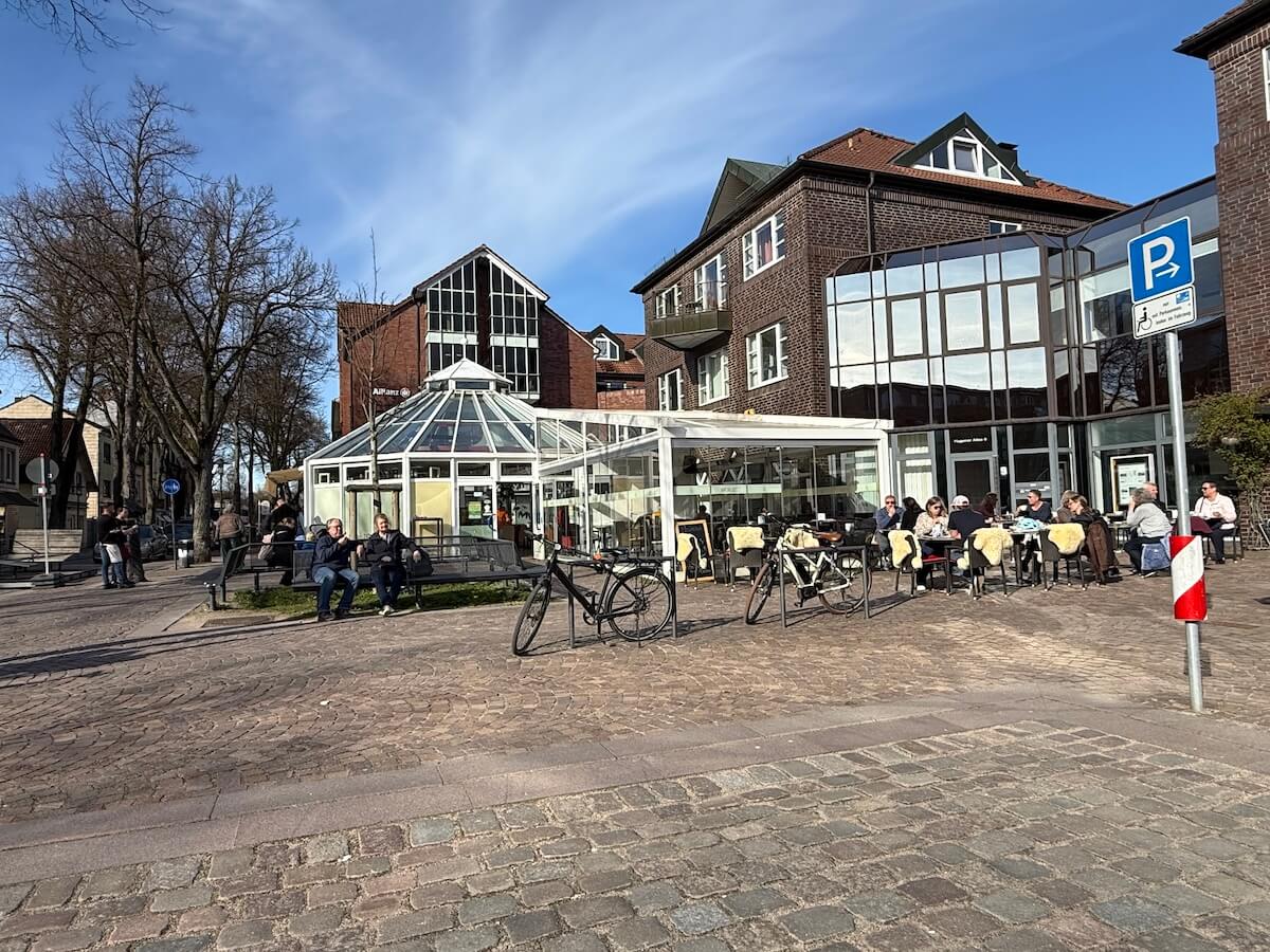 Gebäude und ein Pavillon aus Glas, davor sitzen Menschen auf Stühlen