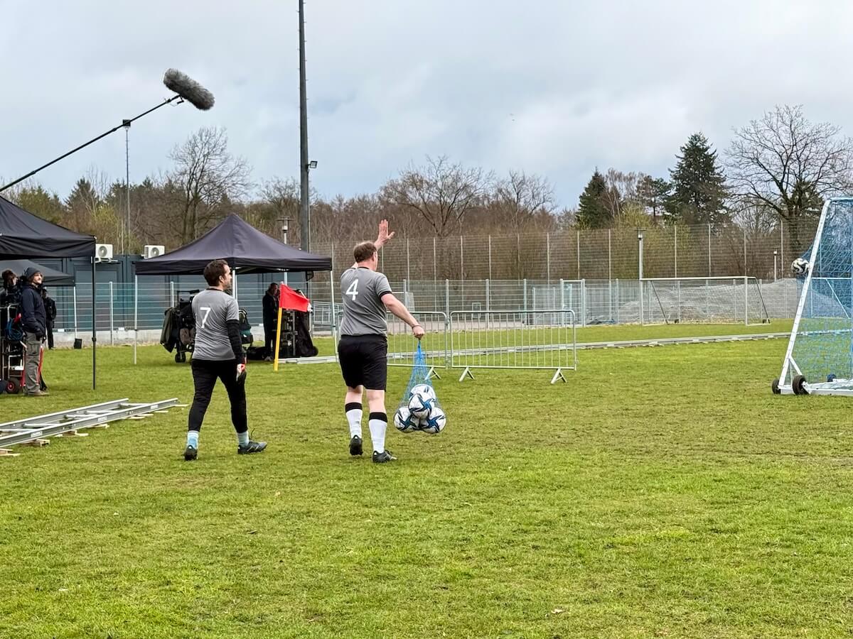 Zwei Männer in Fußballkleidung laufen über das Spielfeld, begleitet von einem Filmteam