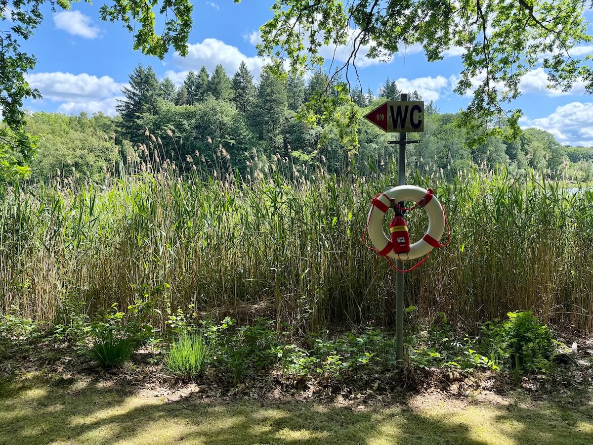 Wegweiser an einem See zum WC, darunter ein Rettungsring