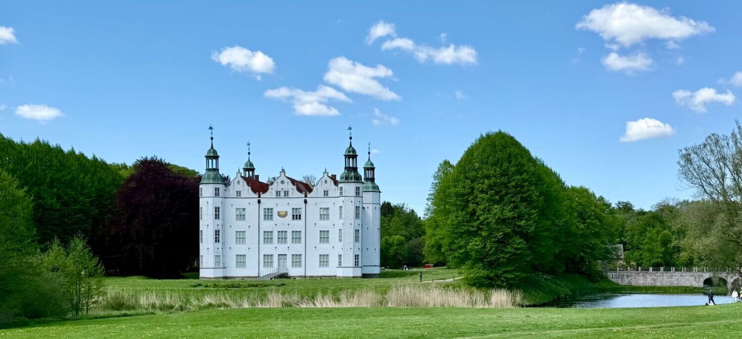 Weißes Schloss im Grünen, blauer Himmel mit wenigen Wolken