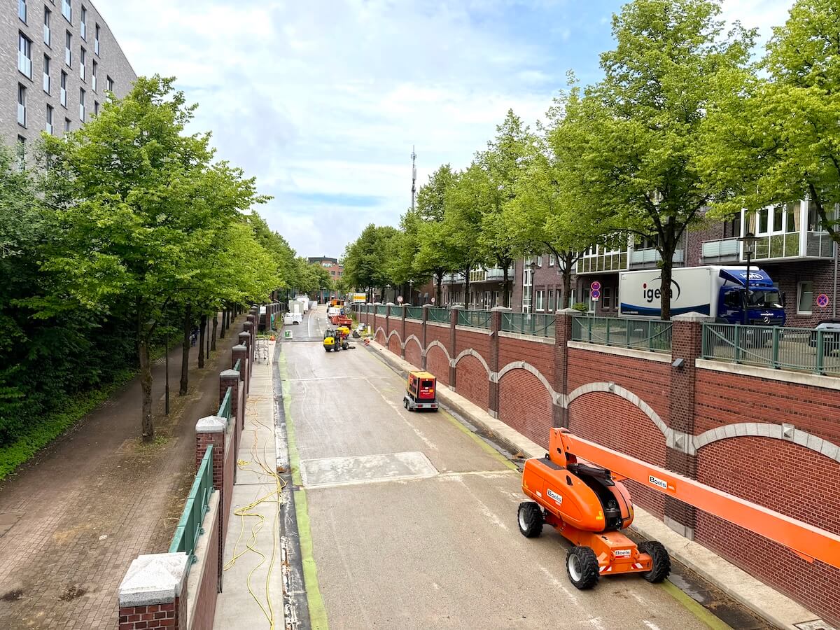 Straße mit Baustellenfahrzeugen, eingerahmt von Bäumen
