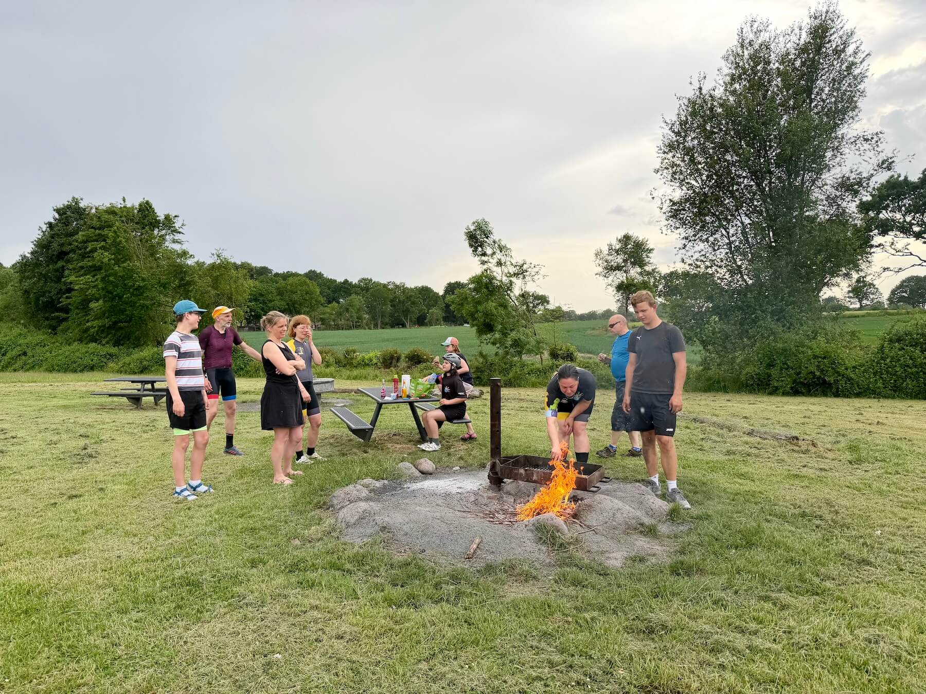 Eine Gruppe von Menschen auf einer Wiese mit Grillstelle am Feuer