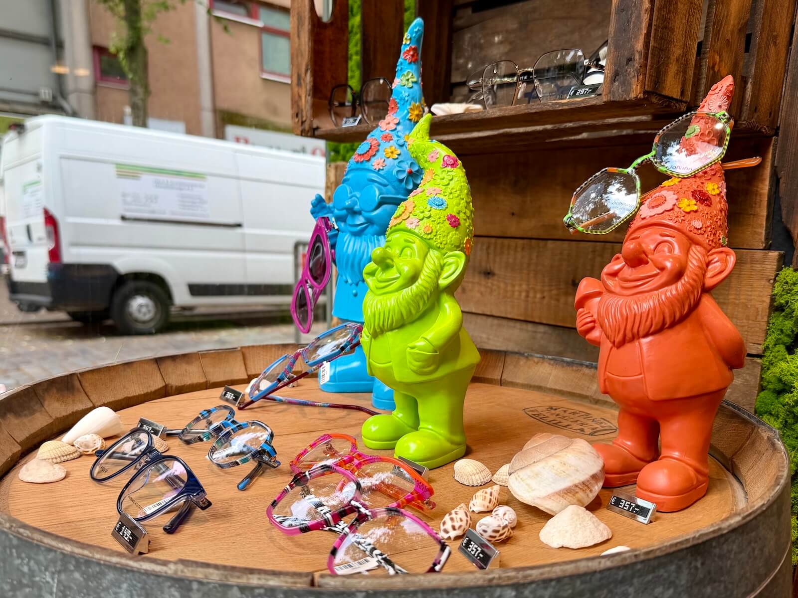 Brillen auf einem Holzfass, daneben bunte Zwerge als Deko