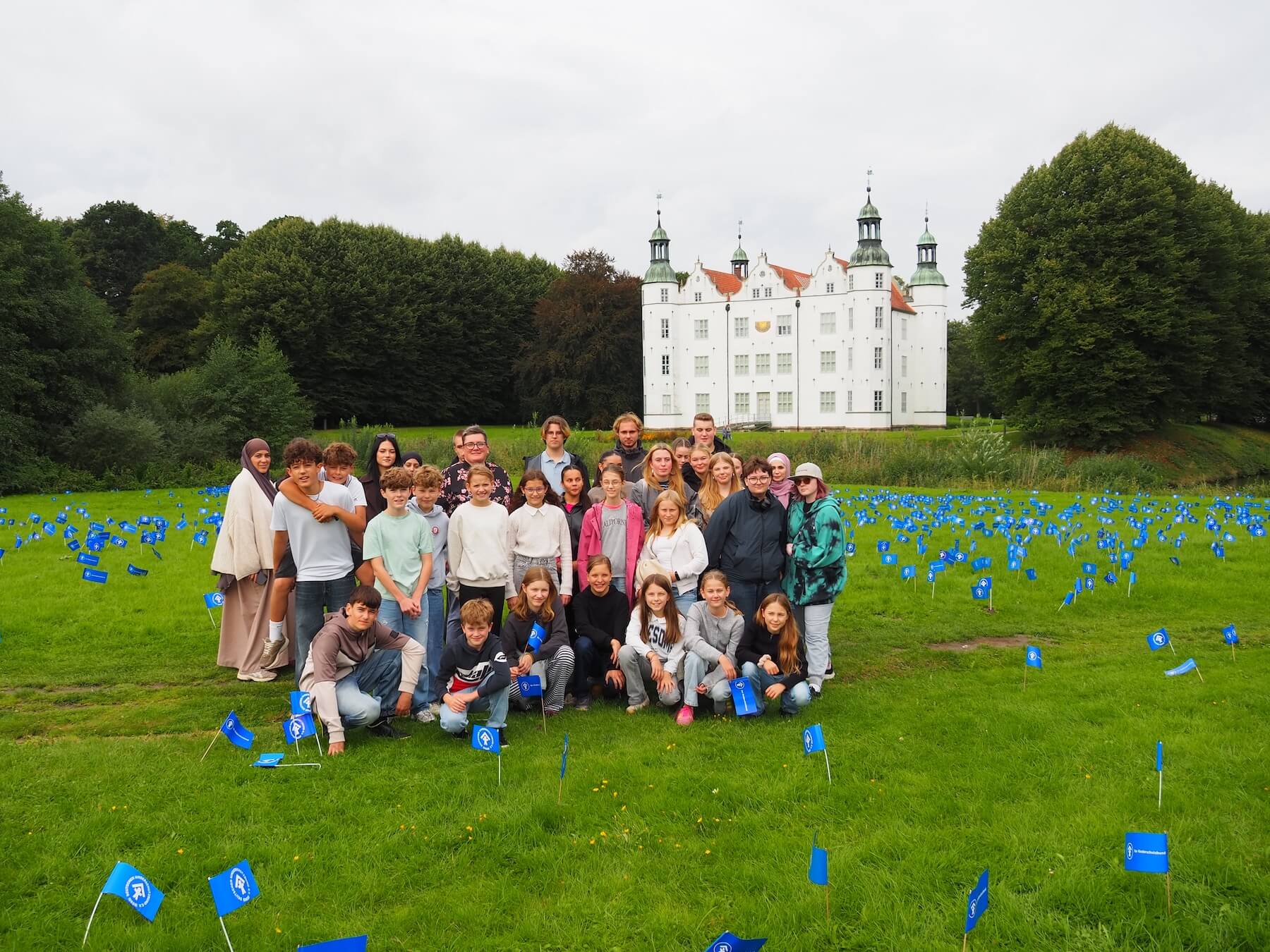 Eine Gruppe Teenager auf einer Wiese vor einem weißen Schloss