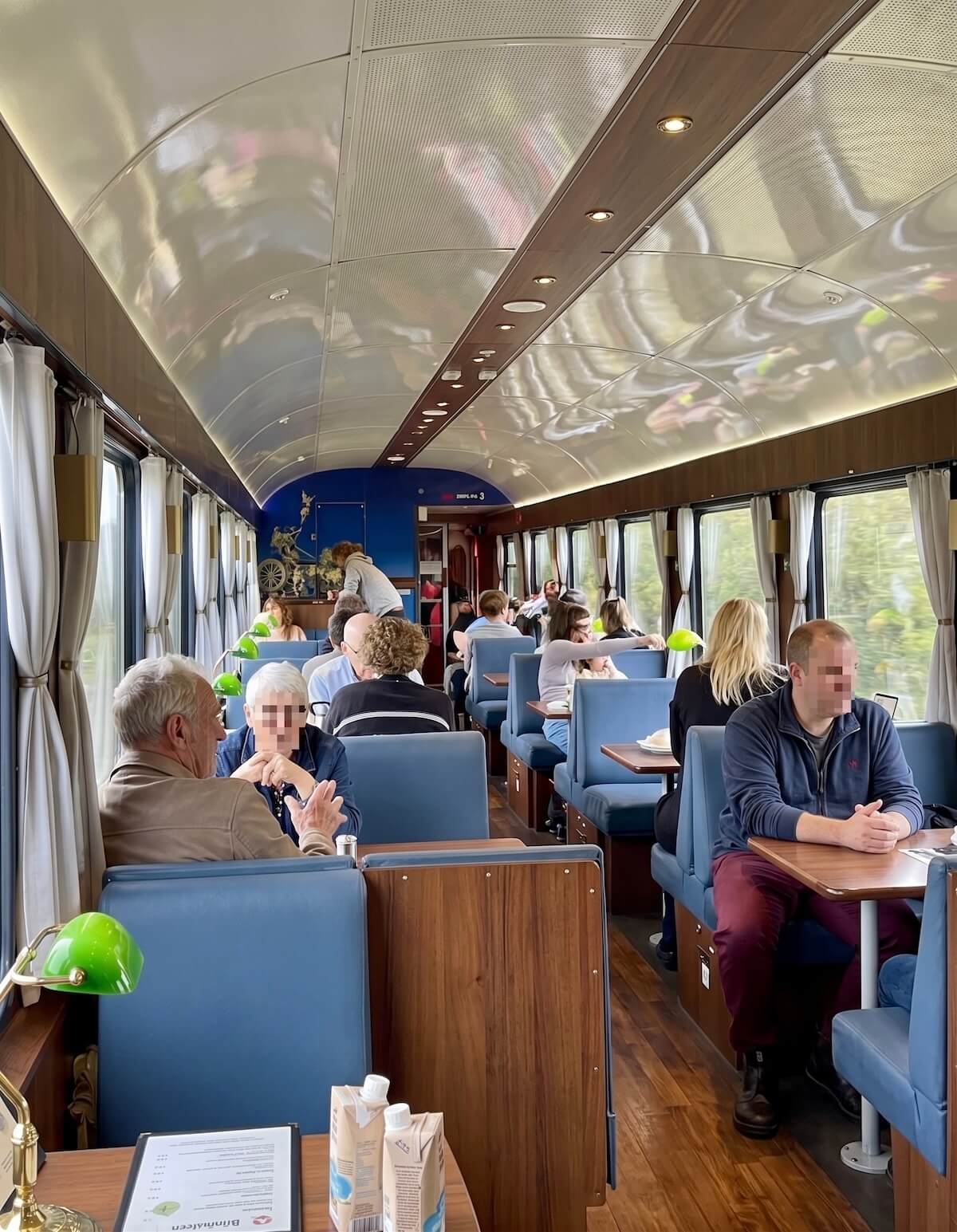 Blick in einen Speisewagen im Zug mit braunen Tischen, blauen Sitzen